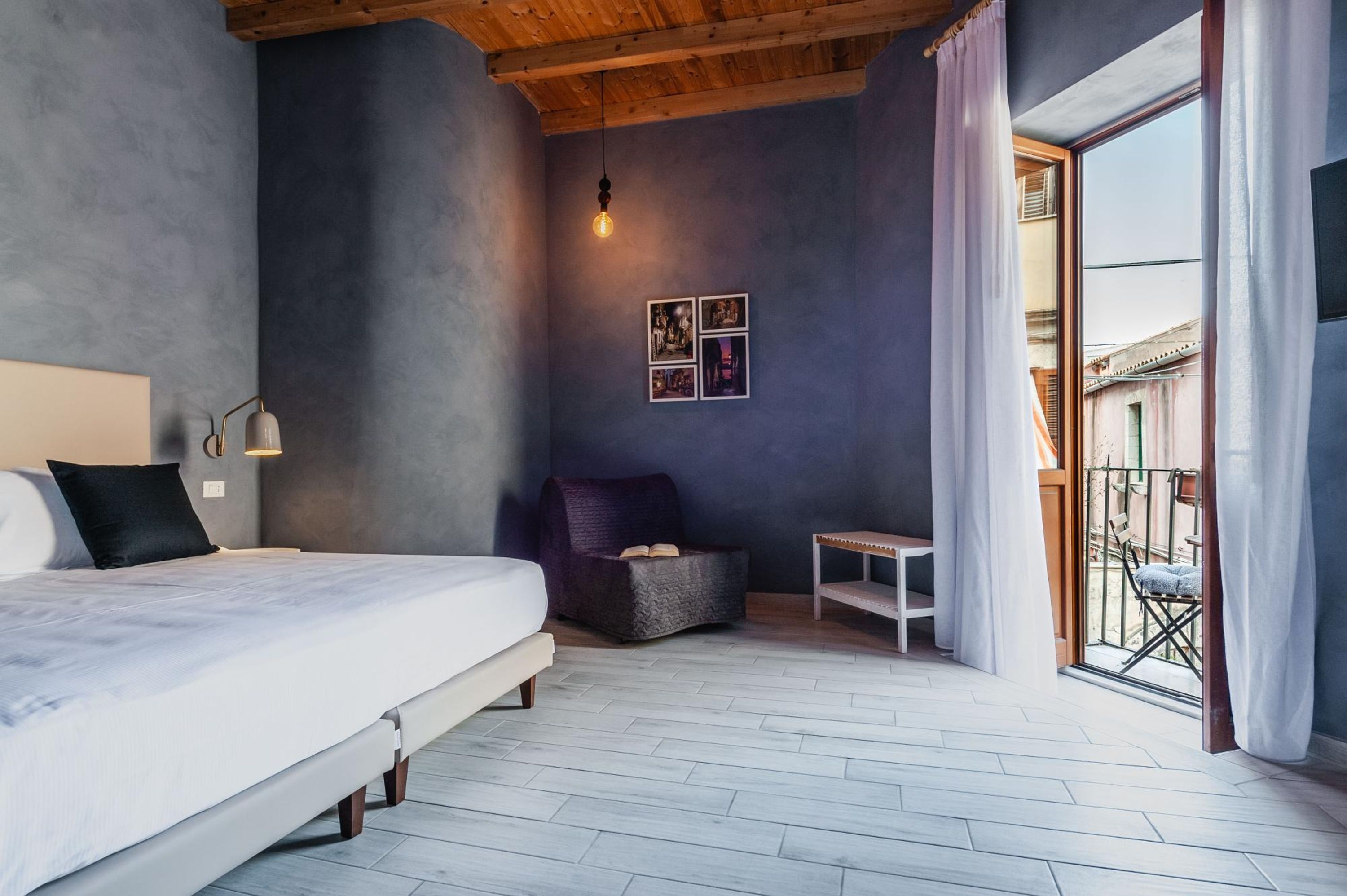 A bedroom with a bed, a small table, a chair, a hanging light, and a balcony with a view.