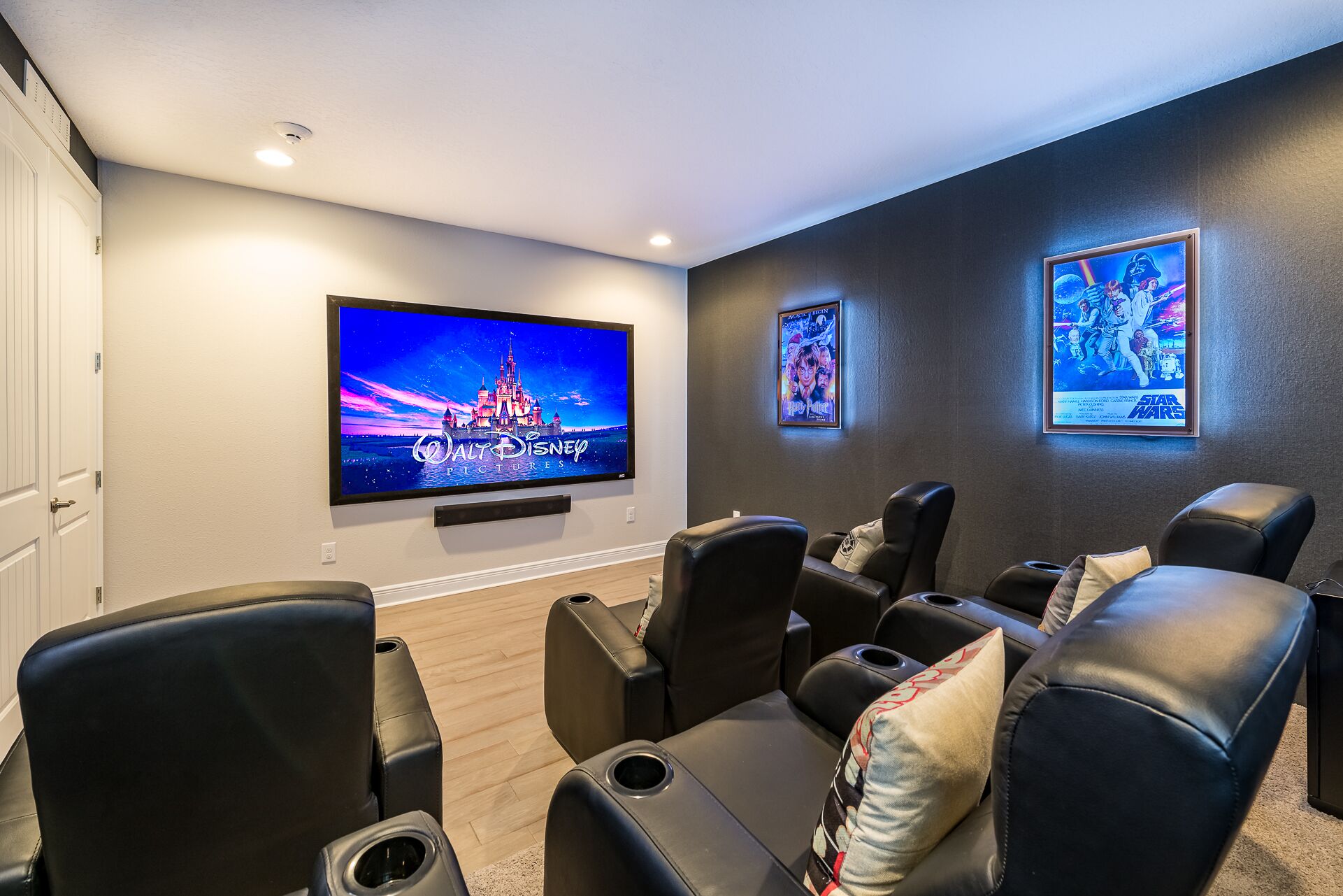 A home theater room with a large flat-screen TV, comfortable leather seating, and framed posters on the wall.