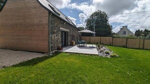 Un edificio de piedra con un añadido de madera, un patio con mobiliario exterior y un patio vallado.