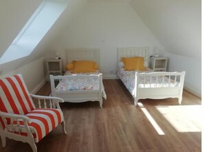 Un dormitorio pequeño y luminoso en el ático con dos camas individuales, una silla a rayas y un tragaluz.