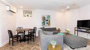 A modern living room with a grey sofa, a round dining table with chairs, a ceiling fan, and a flat-screen TV on a wooden stand. - Chic Condo Near Cedar Point (Sandusky)