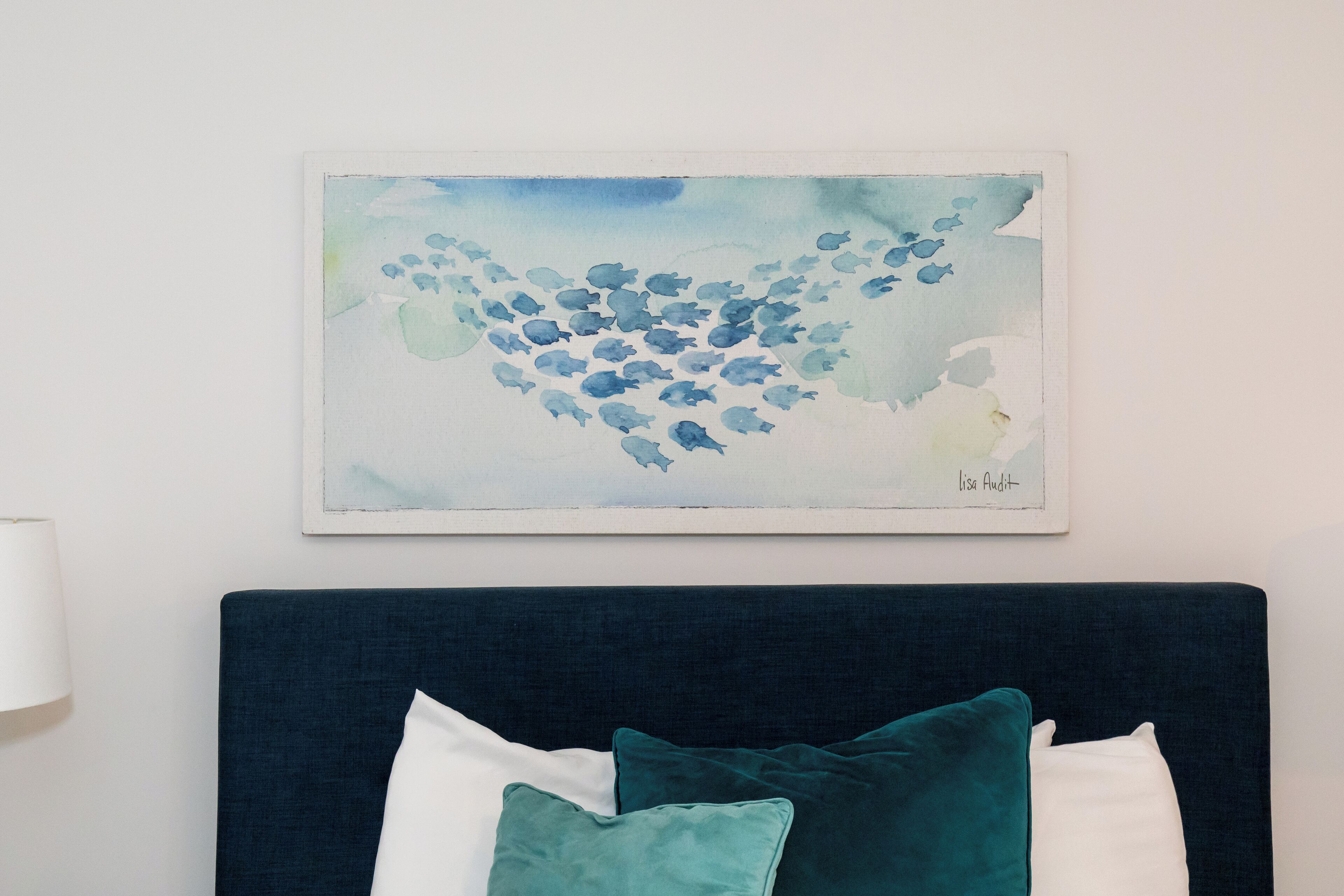 Une chambre avec une tête de lit bleu foncé, des coussins turquoise et blancs, et un tableau à l’aquarelle représentant des poissons accroché au mur.