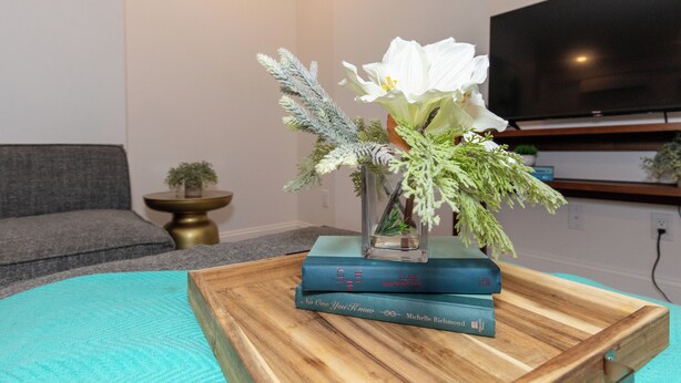 A living room with a wooden coffee table, a vase with flowers, and books. - Chic Condo Near Cedar Point (Sandusky)