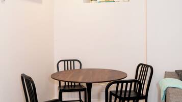 A dining area with a round table and four chairs, an air conditioning unit, a small window with plants, and a herringbone-patterned floor.