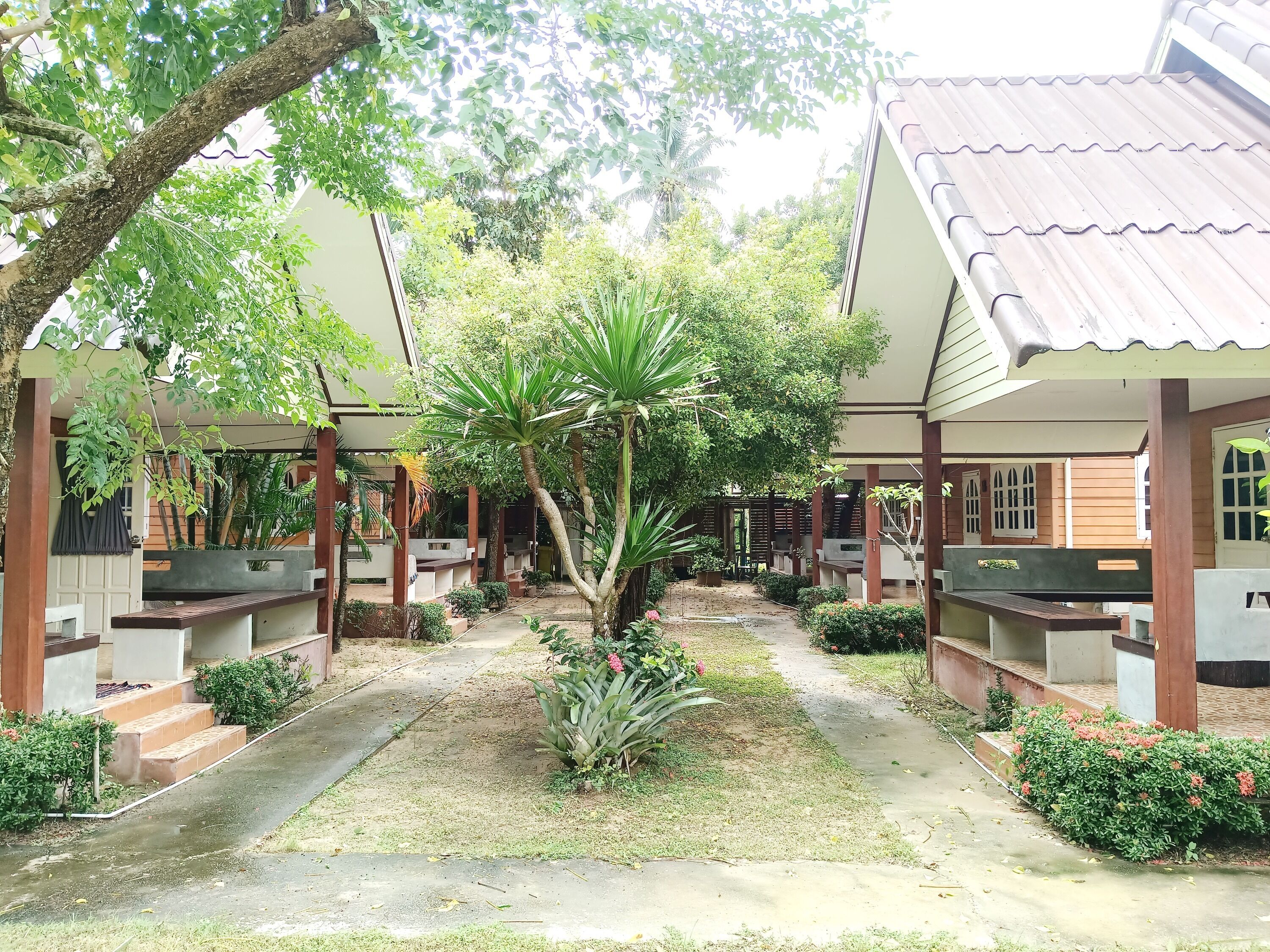 A courtyard with covered seating areas, a central pathway, and surrounding greenery.