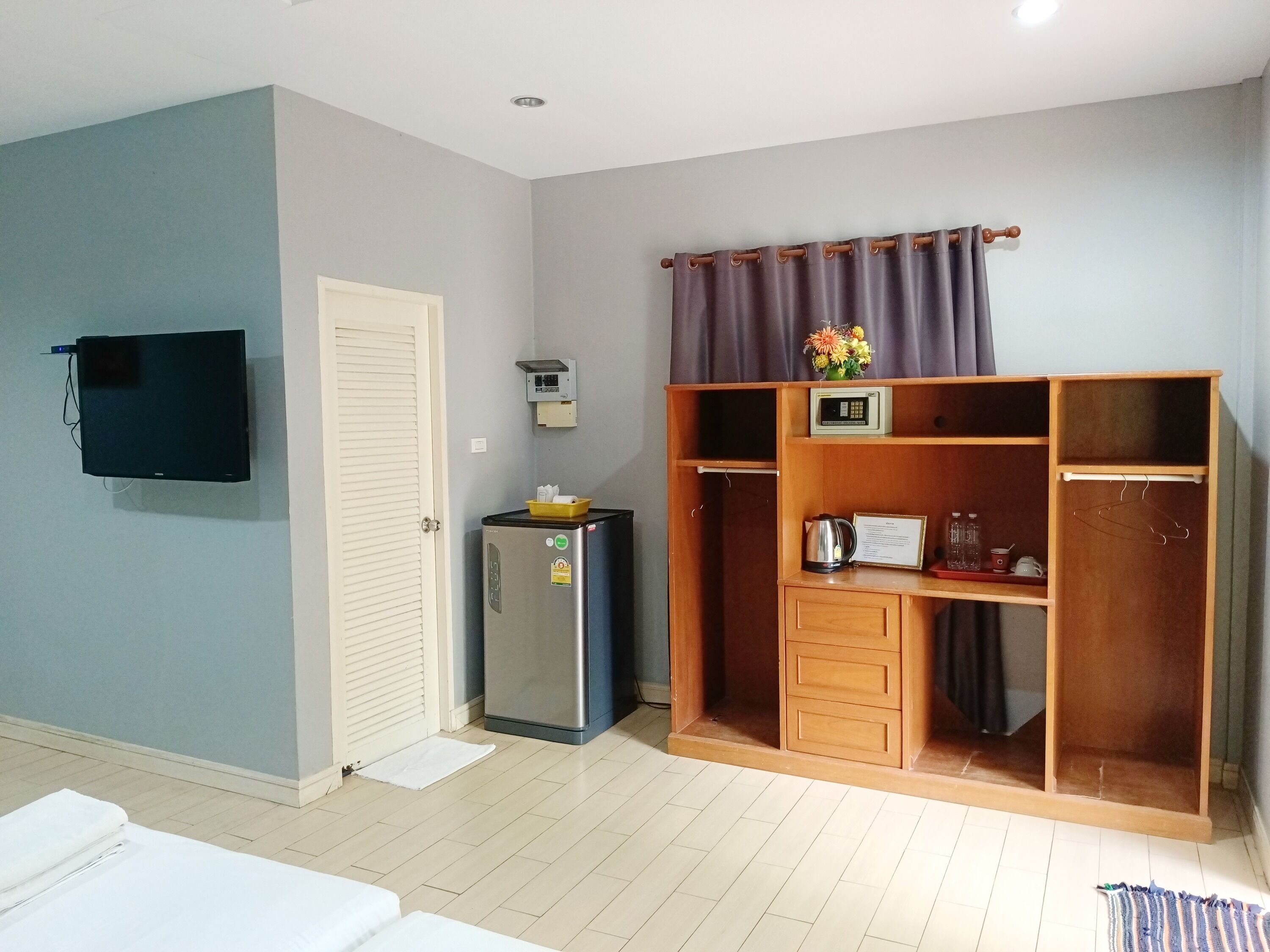 Ein Zimmer mit einem Bett, einem Kühlschrank, einer Mikrowelle, einem Holzschrank und einem an der Wand befestigten Fernseher.