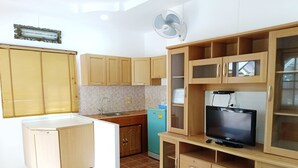 A compact kitchen with wooden cabinets, a built-in refrigerator, a microwave, and a TV on a wooden stand. - Sunrise Resort (Bang Saphan)