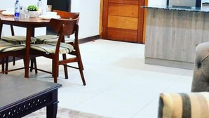 A dining area with a table and chairs, a wooden door, and a kitchen area with cabinets and a refrigerator. - Lux Suites Silverstone  Apartments (Nairobi)