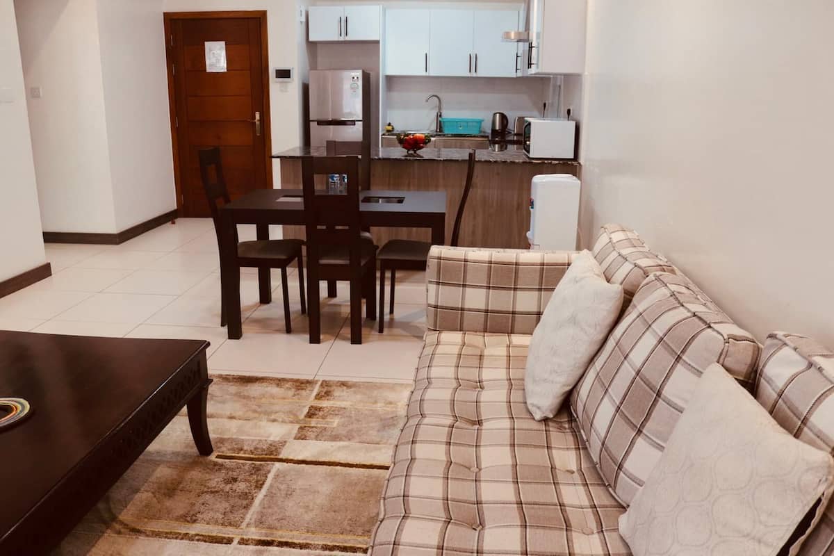A living room with a sofa, a dining table with chairs, and a kitchen area with cabinets and appliances.