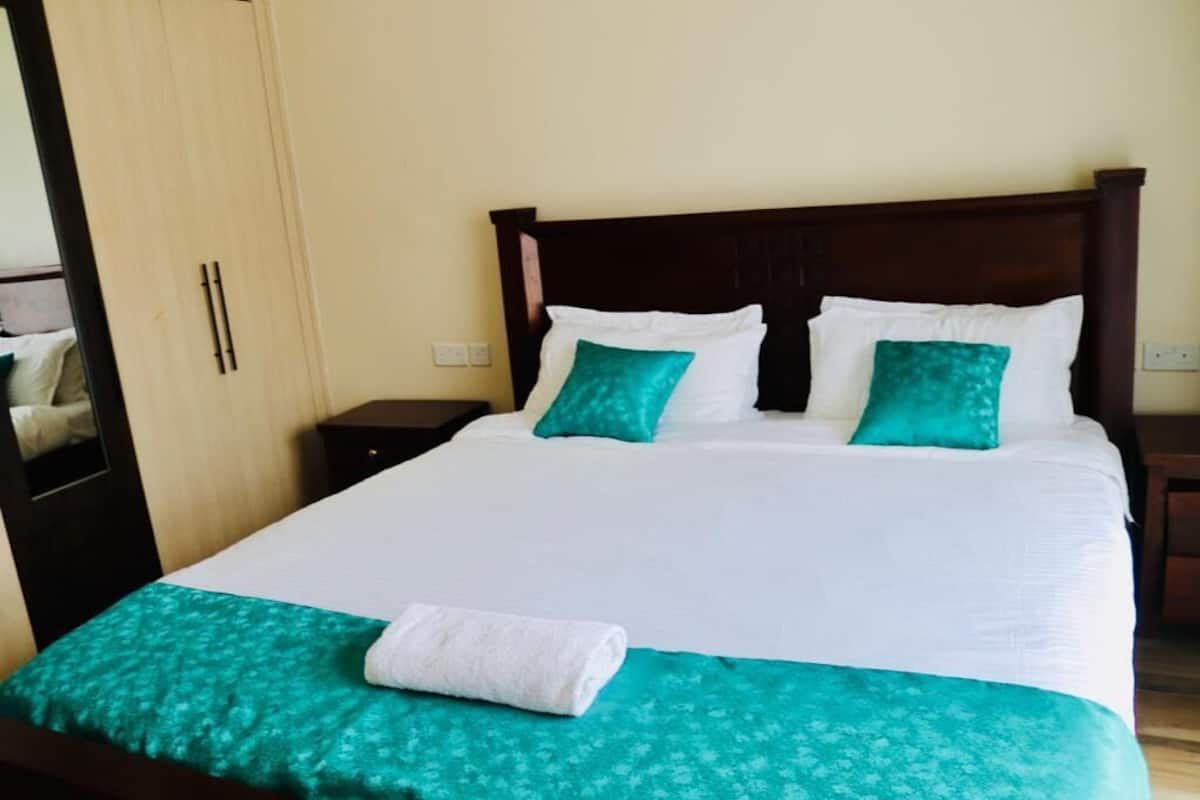 A neatly made bed with white and teal bedding, a wooden headboard, and a teal-patterned bedspread.