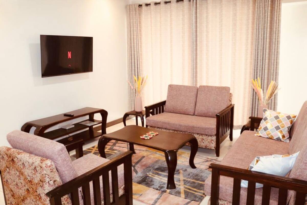 A living room with a sofa, armchairs, a coffee table, and a TV mounted on the wall.