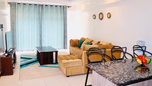 A modern living room with a sofa, ottoman, and a dining area with chairs and a table. - Lux Suites Silverstone  Apartments (Nairobi)