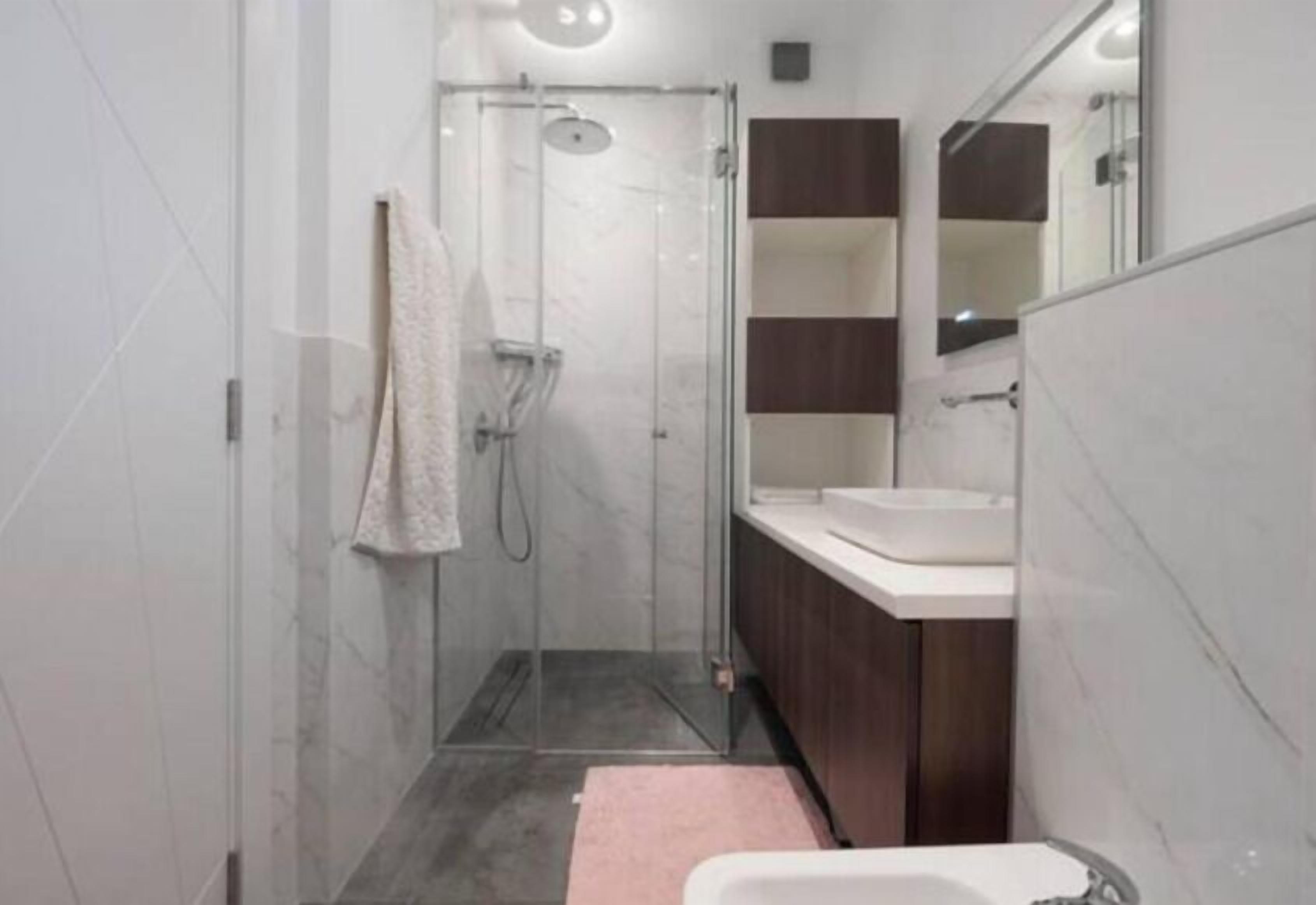 Un baño moderno con ducha acristalada, lavabo blanco y un espejo grande.