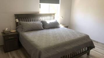 A bedroom with a bed, a nightstand, a lamp, and a window.