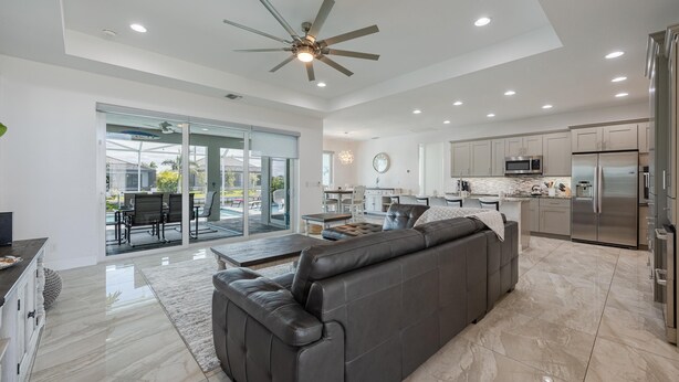 A spacious living area with a dark leather sofa, a ceiling fan, and a modern kitchen with stainless steel appliances. - BRAND NEW - Pool overlooking canal, Outdoor Grilling station - Villa Hummingbird House - Roelens (Cape Coral)