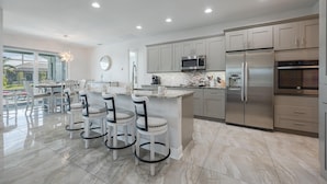 A modern kitchen with a central island, stainless steel appliances, and a dining area with bar stools. - BRAND NEW - Pool overlooking canal, Outdoor Grilling station - Villa Hummingbird House - Roelens (Cape Coral)