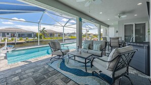 A covered outdoor area with a pool, seating, and a view of a residential neighborhood. - BRAND NEW - Pool overlooking canal, Outdoor Grilling station - Villa Hummingbird House - Roelens (Cape Coral)
