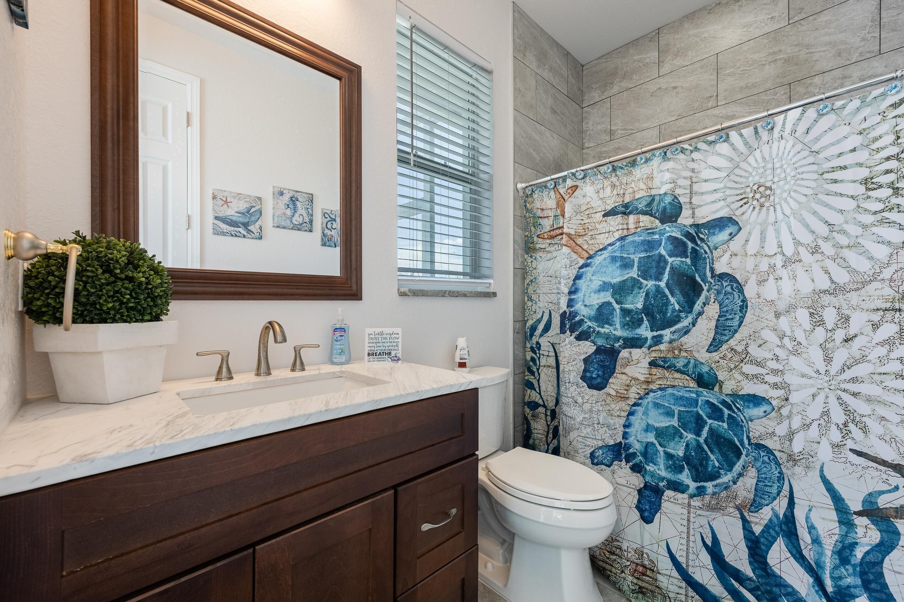 A bathroom with a marble sink, dark wooden cabinets, a white toilet, and a sea turtle mural on the wall.