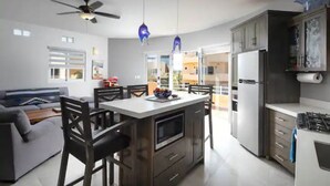 Une cuisine moderne avec des meubles de couleur sombre, un îlot central et un coin repas comprenant un canapé et des chaises.