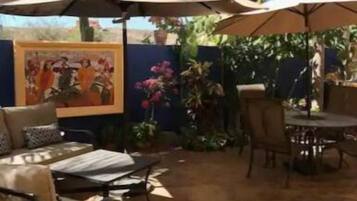 An outdoor patio area with a dining table and chairs, surrounded by palm trees and a mural on the wall.