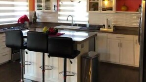 Een moderne keuken met een centraal eiland, barkrukken en een roestvrijstalen koelkast.