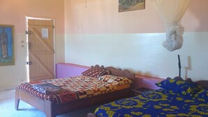 A room with two wooden beds, a hexagonal tiled floor, a door, and a wall-mounted painting. - Pieds Dans L'eau : Grand Studio Avec 2 Lits Double et Terrasse Devant L'océan (toubab dialaw)