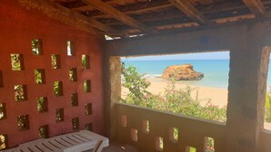 A room with a view of a beach and ocean, featuring a bench and a stone wall with small windows. - Pieds Dans L'eau : Grand Studio Avec 2 Lits Double et Terrasse Devant L'océan (toubab dialaw)