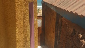 A narrow alleyway with textured walls and a tiled floor, leading to a building with a corrugated metal roof. - Pieds Dans L'eau : Grand Studio Avec 2 Lits Double et Terrasse Devant L'océan (toubab dialaw)