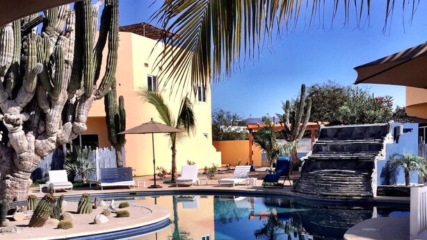 A swimming pool with a clear view of the surrounding area, including cacti and palm trees, and a building with a yellow facade. - 8AP Beautiful 1st Floor Condo, Pool Side, Cerritos
 (El Pescadero)
