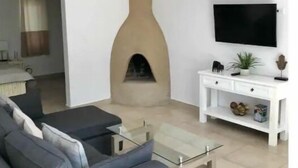 Ett modernt vardagsrum med en soffa, ett soffbord, en tv, en öppen spis och ett vitt konsolbord.