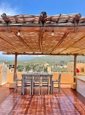 En udendørs terrasse med et bord og stole, en pergola over hovedet og udsigt til bybilledet.