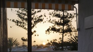 A balcony with a view of trees and a sunset. There are two chairs and a small table.