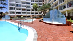 A hotel with a swimming pool, multiple balconies, and a tiled patio area.