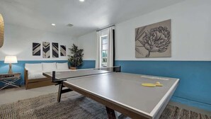 A room with a ping pong table, a bed, a lamp, and artwork on the walls.