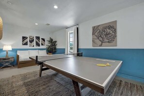 Une pièce avec une table de ping-pong, un lit, une lampe et des œuvres d’art accrochées aux murs.