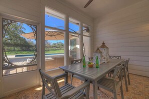 Eine Terrasse im Freien mit Tisch und Stühlen, großen Fenstern und Blick auf Pool und Grünflächen.