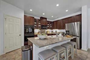 A modern kitchen with dark wood cabinets, stainless steel appliances, and a central island with bar stools.