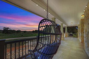 A hanging chair on a balcony with a view of a sunset over a field.
