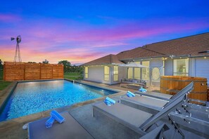 A modern outdoor pool area with lounge chairs, a wooden deck, and a hot tub.