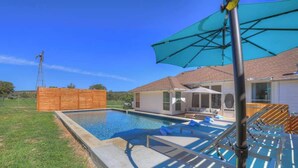 A swimming pool with lounge chairs and a patio umbrella, surrounded by a wooden fence and a house.