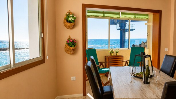 A dining area with a view of the sea, a table with chairs, and two wall-mounted baskets with flowers. - The Waves · Natural Pools & Sea Views, El Pris (El Pris)