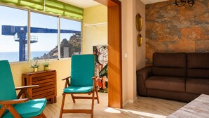 A room with a view of the sea, a wooden bench, a green chair, a brown sofa, and a stone wall. - The Waves · Natural Pools & Sea Views, El Pris (El Pris)
