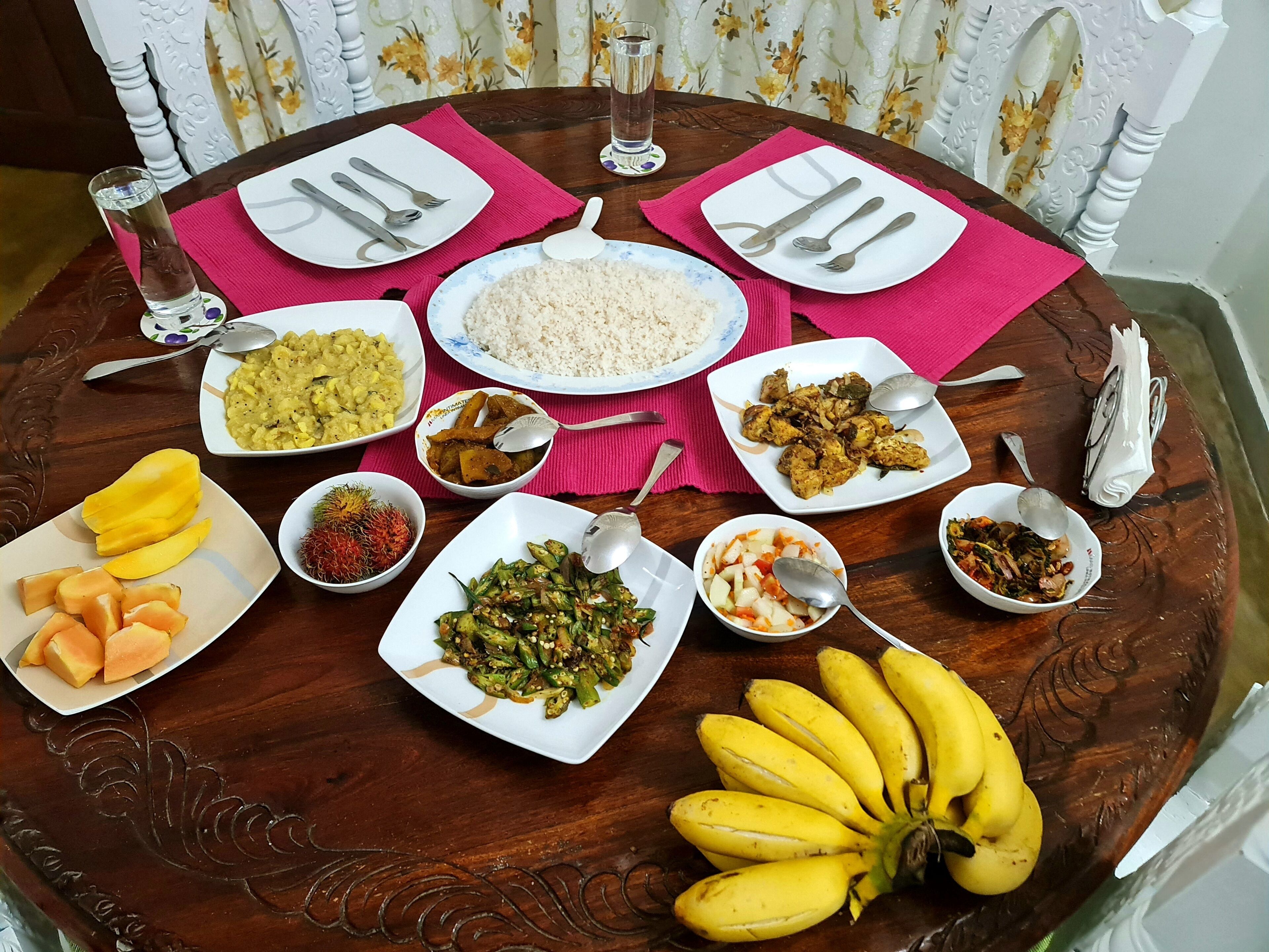 A round dining table with various dishes and utensils, surrounded by chairs with floral curtains.