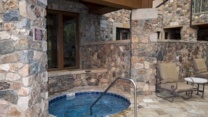 A stone-walled outdoor hot tub area with a metal ladder, stone tiles, and a chair. - Mccoy Peak Lodge #107 1 Bedroom Condo by RedAwning (Avon)