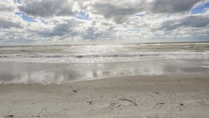 A beach with a wide sandy shore and gentle waves. - Sandy Shores Condo Across From Johns Pass! (Madeira Beach)