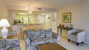 A living room with a sofa, armchairs, a wooden coffee table, and a dining area with chairs and a table. - Sandy Shores Condo Across From Johns Pass! (Madeira Beach)