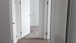 Ein schmaler Korridor mit Holzboden und weißen Wänden, der zu einem Raum mit einer Tür am Ende führt.