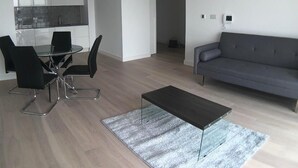 Ein modernes Wohnzimmer mit einem grauen Sofa, einem Glastisch mit vier Stühlen und einem Couchtisch.