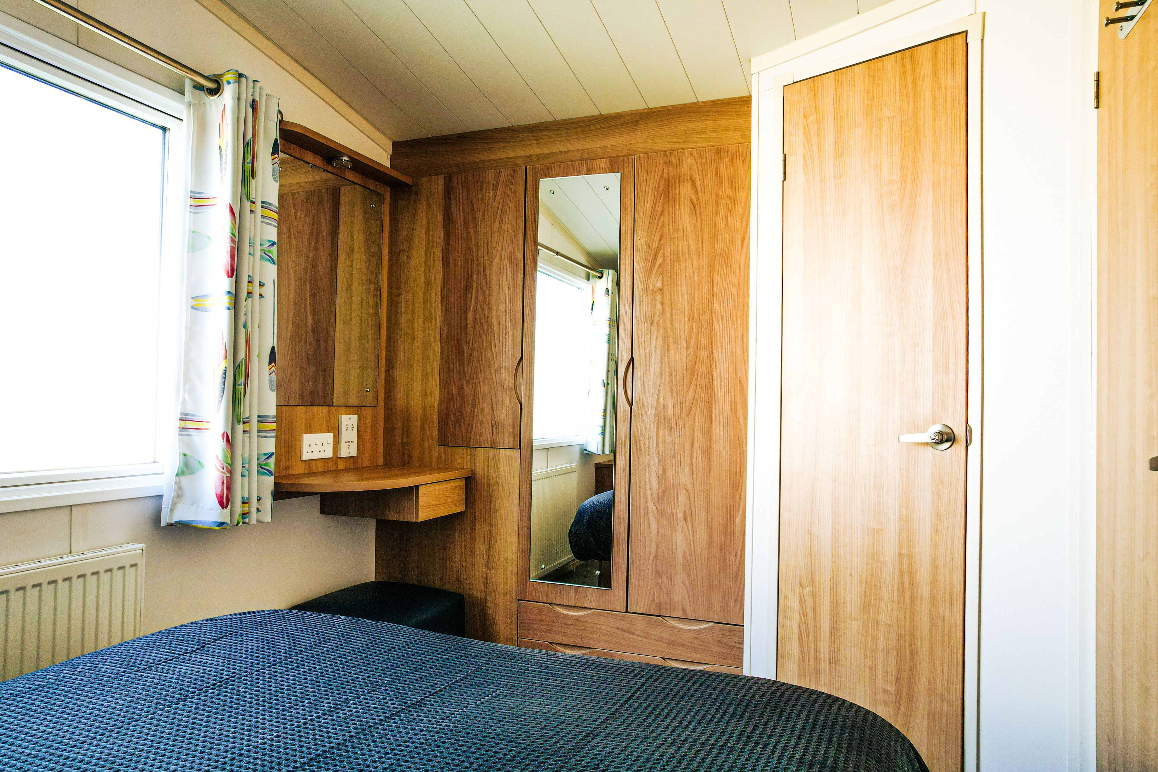 A compact bedroom with a bed, a wardrobe, a mirror, and a window with curtains.