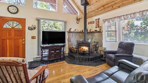 A cozy living room with a stone fireplace, wooden ceiling, and a television.